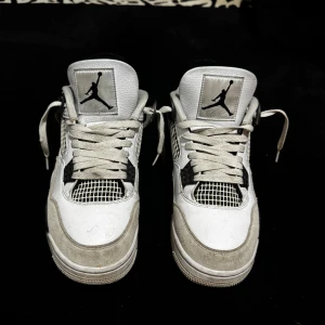Nike Air Jordan 4 Retro Military Black - Säljer ett par Nike Air Jordan 4 Retro i vitt och svart med klassisk Jumpman-logga på plösen och hälen. Skorna har meshpaneler, snörning och detaljer i mocka och skinn. Snygg och ikonisk siluett som passar perfekt till streetwear. Kan cleana dem om det behövs innan jag skickar dem.
