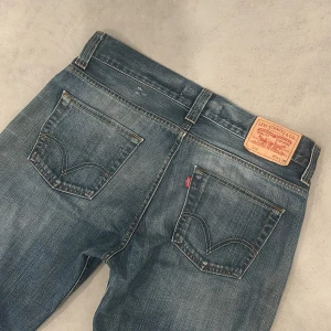 Levi's 506 blå jeans straight fit - Klassiska Levi's 506 jeans i blå tvätt med raka ben och normal passform. Jeansen har fem fickor, bälteshällor och snygga slitningar för en avslappnad look. Tillverkade i slitstarkt denim med Levi's ikoniska läderpatch bak i midjan. 36 i längd så den är ganska långa🙌🏽passar någon som är 185+