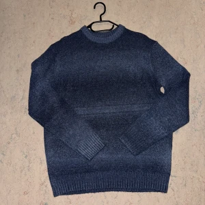 Mörkblå stickad tröja med rund hals - Mysig mörkblå stickad tröja med rund halsringning och ribbade muddar vid ärmslut och nederkant. Perfekt för kyliga dagar och enkel att matcha med jeans eller kjol. Klassisk modell med lång ärm och mjukt material.