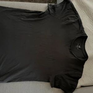 Svart crewneck t-shirt från H&M - En svart basic crewneck t-shirt från H&M i regular fit. T-shirten har korta ärmar och är gjord i mjuk bomull, perfekt för en clean och enkel stil. Passformen är normal och den funkar till allt när du vill hålla det stilrent.