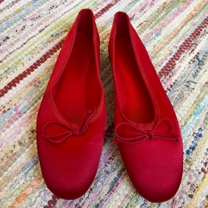 Röda ballerinaskor från H&M, strl 36 - Snygga röda ballerinaskor från H&M i satinliknande material. Skorna har rund tå, platt sula och en söt rosett framtill. Trendig modell! Använda en gång. Stl 36, true to size. 
