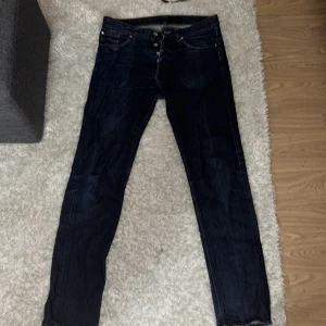Mörkblå tiger of sweden jeans 30/34 - Snygga mörkblå jeans från Alex i modellen Serene Blue. Klassisk femficksdesign med knappgylf och raka ben. Jeansen har kontrastsömmar och en läderpatch bak i midjan. Perfekt passform för dig som gillar stilrena och tidlösa jeans.