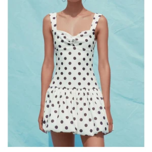 Vit kortprickig klänning med volangkjol - Supersöt vit kort klänning med svarta prickar och breda axelband. Fint skick! 