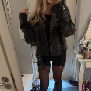 Svart oversized skinnjacka med bälte - Säljer en svart oversized skinnjacka med coola detaljer som dragkedjor vid ärmslut och fram, samt ett bälte i midjan. Jackan har breda slag, fickor med lock och en loose passform som ger en edgy vibe. Perfekt för dig som gillar streetstyle och vill sticka ut. skinn/läder jacka använd nån gång bara💕 nypris 599kr