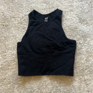 Svart sportig linnetopp från H&M - Säljer en svart, ribbad linnetopp från H&M Sport i storlek XS. Toppen har en hög halsringning och är ärmlös, perfekt för träning eller chill dagar. Materialet är stretchigt och följsamt för extra komfort men mycket bra support med paddar! Kontakta för fler bilder🩷