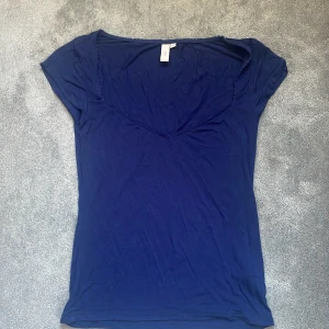 Mörkblå topp med v-ringning från Nelly - Säljer en mörkblå topp från Nelly i storlek S. Toppen har en djup v-ringning och korta ärmar. Materialet är mjukt och stretchigt, perfekt för en avslappnad look. Enkel och stilren design som är lätt att matcha med olika outfits.