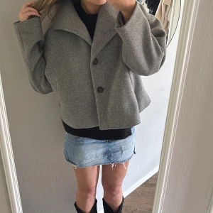 Grå kappa från Noisy May - Snygg grå kappa från Noisy May med klassisk krage och två knappar framtill. Jackan har raka fickor på sidorna och är tillverkad i ett mjukt ull-liknande material. Perfekt för dig som gillar stilrena och minimalistiska plagg.