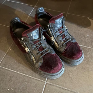 Vinröda sneakers från Giuseppe Zanotti - Säljer ett par unika sneakers från Giuseppe Zanotti i vinröd sammet och svart skinn. Skorna har coola dragkedjor på sidorna, snörning och en chunky svart sula. Perfekta för dig som vill sticka ut med stilrena detaljer och lyxig känsla.