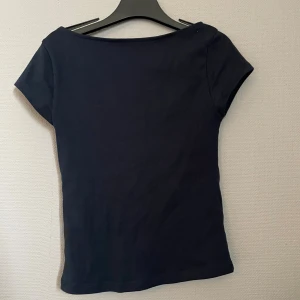 Svart croppad topp från Gina Tricot - En svart croppad topp från Gina Tricot med korta ärmar och djup rundad urringning bak. Enkel och stilren design i mjukt bomullsmaterial, perfekt att matcha med jeans eller kjol. Snygg passform som sitter tajt mot kroppen.💕💕