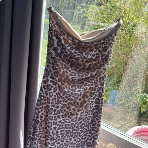 Leopardmönstrad långklänning med tunna band - Snygg långklänning med leopardmönster och tunna axelband. Klänningen har en draperad urringning och är i ett lätt, följsamt material som ger en cool och trendig look. Perfekt för dig som vill sticka ut med ett djurmönster. Aldrig använd 