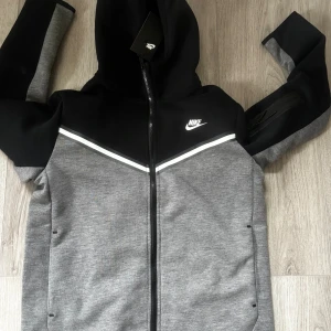 Nike tech grå svart - Nike tech som säljs helt ny då den ej passade när jag fick den, storleken på den är L men skulle säga att den passar någon som har M i storlek👍🏻