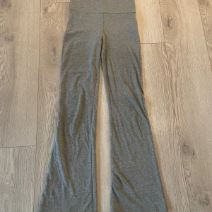 Grå bootcut byxor från Gina Tricot - Grå mjuka bootcut byxor från Gina Tricot med bred linning som kan vikas ner. Byxorna är i stretchigt material och har en snygg, avslappnad passform med utsvängda ben. Perfekta för en chill och trendig look.