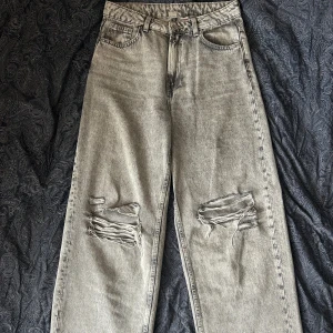 Grå ripped jeans från H&M  - Säljer ett par grå jeans från H&M Divided i storlek 36. De har en loose fit med raka ben och slitna detaljer över knäna för en cool, avslappnad vibe. Klassisk femficksmodell och tillverkade i jeansmaterial. Perfekta för dig som gillar en trendig streetstil.