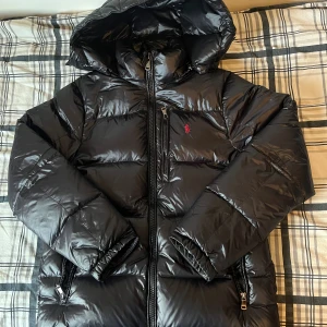 Ralph lauren pufferjacka - Säljer en svart pufferjacka från Ralph Lauren med huva och dragkedjor. Jackan har glansig finish, klassisk röd logga på bröstet och flera fickor med dragkedja. Den har avtagbar luva och är i hög kvalitet. Köpte den förra vintern men har inte använt den så mycket då de inte är så kallt i Skåne. 9/10 skick, orderbekräftelse finns! Skriv om ni har frågor!