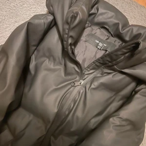 Svart pufferjacka från Vero Moda - Säljer en svart pufferjacka från Vero Moda med huva och dragkedja framtill. Jackan är vadderad och har en oversized look, perfekt för kalla dagar. Materialet är syntet och jackan har långa ärmar. Enkel och stilren design. Nästan aldrig använd! Köpt för 900kr