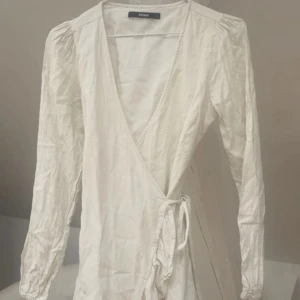 Vit omlottklänning från Bikbok - Supersöt vit/creme färgad omlottklänning i linne med  volangkant nedtill. Klänningen har v-ringad hals och knyts i midjan, endast använd 1 gång💕