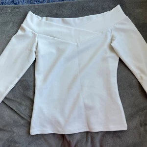 Vit offshoulder topp från H&M - Säljer en stilren vit offshoulder topp från H&M i storlek XS. Toppen har långa ärmar och en bred, v-formad kant upptill som ger en snygg och modern look. Perfekt att matcha med jeans eller kjol för en trendig outfit.