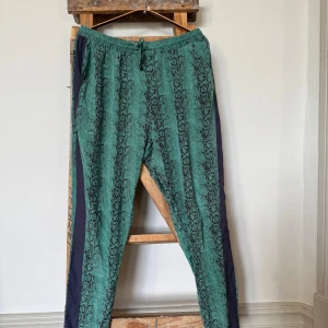 Grön byxa i elastisk siden med ormmönster - Grön byxa i elastisk siden med ormmönsters och mörka sidopaneler. Byxorna har elastisk midja med snörning och fickor på sidorna. 