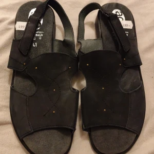 Svarta sandaler 41stl - Svarta sandaler i skinn från Ace Soft&Flex, tillverkade i Portugal. De har öppen tå, platt sula och justerbar rem med kardborre. Snygga detaljer med små nitar och dekorativa sömmar på ovandelen. Perfekta för varma dagar och enkel att matcha med olika outfits.