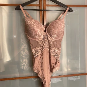 Rosa spets body  - Supersnygg rosa korsettbody från H&M med blommig spets och meshdetaljer. Justerbara axelband och vacker v-ringning framtill. Perfekt för att lyfta din outfit med en feminin touch. Säljes i storlek 42.