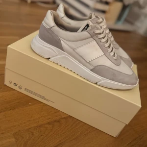 Axel Arigato sneakers  - Snygga sneakers från Axel Arigato i storlek 42. Skorna har en stilren design i beige och vitt med detaljer i mocka och textil. Klassisk snörning och chunky vit sula ger en modern vibe. Perfekta för dig som gillar minimalistisk och clean stil.