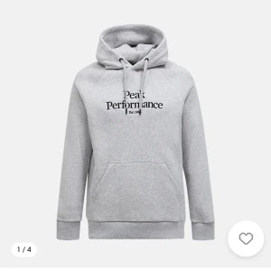 Grå hoodie från Peak Performance - Snygg grå hoodie från Peak Performance med svart logga på bröstet. Tröjan har huva med snörning och en stor magficka. Perfekt för chill dagar eller när du vill ha en sportig look.