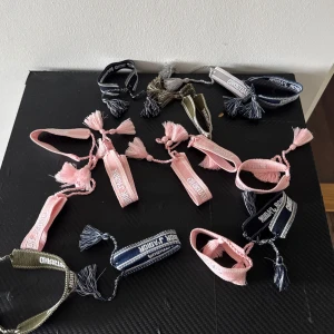 Christian Dior armband  - Flera snygga armband från Christian Dior i olika färger som rosa, blå, grå och olivgrön. Armbanden är vävda med tofsar i ändarna och har märkets logga broderad. Perfekt accessoar för att lyfta din outfit med en lyxig touch.