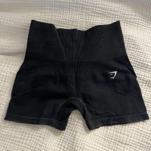 Svarta seamless shorts från Gymshark - Svarta seamless shorts från Gymshark. Stretchigt material som sitter tight och bekvämt, perfekt för träning. Diskret logga i vitt på ena benet. Snygg och sportig look som ger bra stöd. Säljer eftersom kommer ej till använing och är lite tajta på mig🫶 köpta för 499.