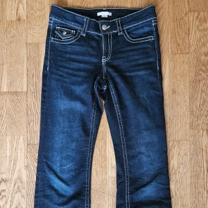 Mörkblå jeans från Gina Tricot, stl 158 - Snygga mörkblå jeans från Gina Tricot med kontrasterande vita sömmar och klassiska fem fickor. Jeansen har låg midja och bootcut- modell. Tillverkade i mjukt denimtyg. 