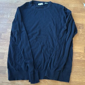 Svart stickad tröja Jack & Jones M - En svart stickad tröja från Jack & Jones i storlek M. Tröjan har rund halsringning, långa ärmar och ribbade muddar vid ärmslut och nederkant. Enkel och stilren modell som passar perfekt till jeans eller chinos.