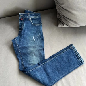 Blå jeans från Jacob Cohen - Snygga blå jeans från Jacob Cohen med klassisk femficksdesign och rosa patch bak. Jeansen har raka ben och subtila slitningar framtill för en cool look. Passar dig som gillar stilrena detaljer och kvalitetsjeans.