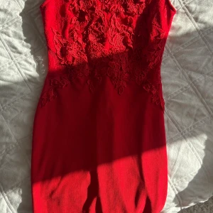 Röd spetsklänning från Lipsy London - Säljer en snygg röd kortklänning från Lipsy London i storlek 36. Klänningen har vacker spets upptill med blommigt mönster och figurnära passform. Perfekt för dig som vill sticka ut med en färgstark look och coola detaljer.