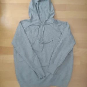 Ljusgrå merinoulls hoodie med snörning - Mysig ljusgrå stickad hoodie i merino ull med huva och snörning framtill. Tröjan har långa ärmar och ribbade muddar vid ärmslut och nederkant. Perfekt för chill dagar eller när du vill ha något bekvämt och stilrent. Priset kan diskuteras vid snabb affär! Fråga gärna frågor om det finns några