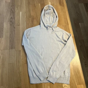 Beige stickad hoodie från RYVLS - Snygg beige stickad hoodie från RYVLS Stockholm. Tröjan har huva med snörning, ribbade muddar och lång ärm. Perfekt för dig som gillar en clean och enkel stil med mjukt material och relaxed fit.
