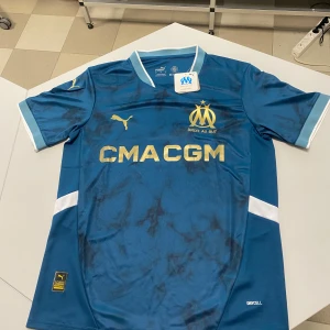 Blå Marseille fotbollströja Puma - Säljer en officiell Olympique de Marseille fotbollströja från Puma. Tröjan är blå med guldiga detaljer och klubbmärke, korta ärmar och vit accent vid ärmslut och sidor. Tillverkad i lätt och ventilerande polyester med DryCell-teknologi.