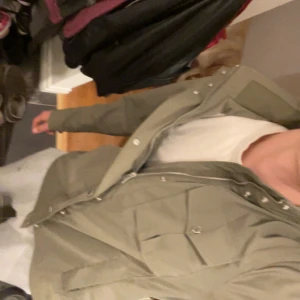 J.Lindeberg Jacka - Säljer en snygg grön vindjacka från J.Lindeberg med flera fickor framtill och diskret logga på ärmen. Jackan har dragkedja och tryckknappar, perfekt för dig som vill ha en stilren och funktionell look. Superbra skick och riktigt snygg!