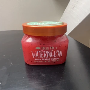 Tree Hut Watermelon Shea Sugar Scrub - En stor burk med Tree Hut Watermelon Shea Sugar Scrub, 510g. Skrubben är rosa med svarta prickar och har en fräsch vattenmelon-doft. Innehåller sheasmör och veganskt kollagen för återfuktad och mjuk hud. Kommer i en plastburk med orange lock och mintgrön etikett. 💓Testade den en gång. Nypris: 399
