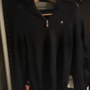 Morris halfzip tröja - Mörkblå stickad tröja från Morris i 100% merinoull med halv dragkedja och hög krage. Tröjan har en liten broderad logga på bröstet och snygga detaljer vid dragkedjan. Perfekt för dig som gillar stilrena och klassiska plagg.