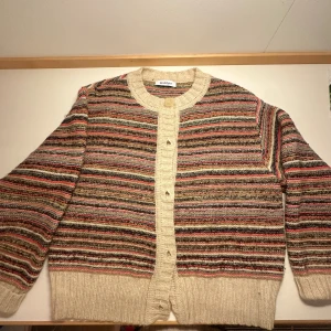 Randig kofta från Rodebjer i ull - Säljer en mysig och färgglad randig kofta från Rodebjer i mjuk ullmix. Koftan har breda ribbstickade kanter i beige, stora knappar framtill och långärmad passform. Färgerna går i beige, röd, grön, blå och bruna toner. Perfekt för lager-på-lager under hösten och vintern. Är storlek m men passar S super