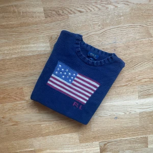 Polo Ralph lauren Amerika edition storlek Small - Snygg mörkblå stickad tröja från Polo Ralph Lauren med amerikansk flagga i vitt, rött och blått på bröstet samt RL-broderi. Rund hals och långa ärmar med ribbade muddar. Perfekt för dig som gillar klassisk och preppy stil. Storlek: S, bra skick, Äkta