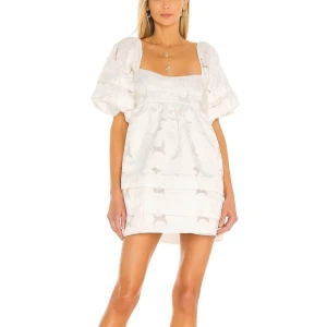 Studentklänning  - Superfin vit kortklänning med puffiga kortärmar och broderade blommor. Klänningen har öppen rygg med knytband och en söt volangdetalj nedtill. Perfekt för sommarens alla tillfällen, med luftig passform och romantisk vibe.