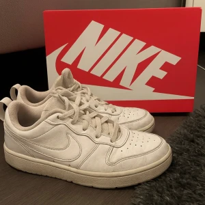 Vita Nike sneakers med snörning - Säljer ett par klassiska vita Nike sneakers med låg profil och rund tå. Skorna har snörning och är tillverkade i skinn med perforerade detaljer på tån för extra ventilation. Perfekta för dig som gillar stilrena och tidlösa sneakers. MVH Lucas