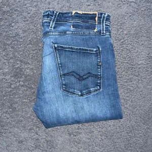 Replay Anbass jeans  - Snygga Replay Anbass jeans i blå tvätt med slim passform. Klassisk femficksdesign, med Replay-logga på bakfickan och slitningar för en cool look. OBS som man ser är patchen ovanför bakfickan sönder men i övrigt mycket bra skick 👍Ifall det inte finns någon bild i annonsen där jag bär plaggen jag säljer så är det för att jag ej kan ha storleken heller passformen, så kolla måtten för storlek och googla på modellnamnet för passform 😉S1