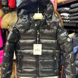 Svart Moncler pufferjacka med huva 36-40 - Säljer en svart pufferjacka från Moncler med glansig finish, huva och dragkedja framtill. Jackan har Moncler-logga på ärmen, två sidofickor med dragkedja och quiltad design. Perfekt för kalla dagar och riktigt snygg streetstil.