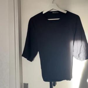 Svart bolerotopp med knyt i midjan - Säljer en svart bolerotopp med rund hals och trekvartsärmar. Toppen har ett snyggt knyt i midjan baktill som ger en cool och modern look. Materialet är i t shirt material perfekt för att styla med jeans eller kjol. Enkel och stilren design som funkar till många outfits.