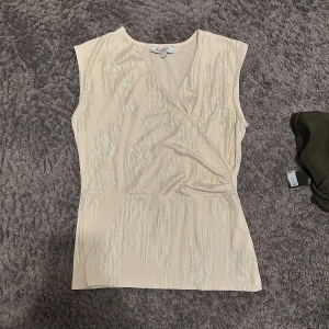 Guldig omlottopp från Morgan - Snygg ljusbeige omlottopp från Morgan med guldiga ränder. Toppen är ärmlös och har en lätt omlott-effekt framtill. Perfekt partytopp eller liknande! Köpt på Zalando!