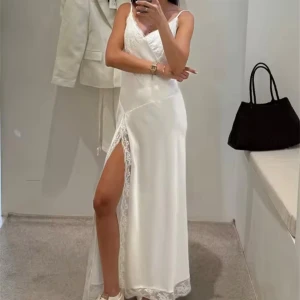 Vit långklänning med spets och slits S-M - Elegant vit långklänning med smala axelband, v-ringning och spetsdetaljer upptill samt längs slitsen. Klänningen har en hög slits på ena sidan och är tillverkad i ett glansigt, satinliknande material. Perfekt för dig som vill ha en stilren och feminin look.