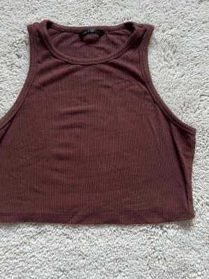 Brun ribbad croppad linnetopp från SHEIN - Säljer en brun croppad linnetopp från SHEIN i storlek S. Toppen är ribbad och ärmlös med rund halsringning.  Materialet är mjukt och stretchigt för en bekväm passform. Är använd ett par gånger💓