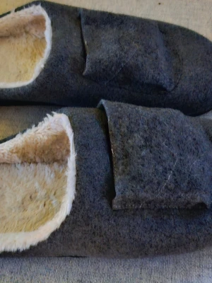 Grå värmesulor med fuskpäls - Mysiga grå värmesulor med mjukt fuskpälsfoder och batteridriven värmefunktion. Perfekta för kalla dagar hemma eller på kontoret. Sulorna har en enkel design med rund tå och platt sula, och värmeelementet göms under en ficka på ovansidan.