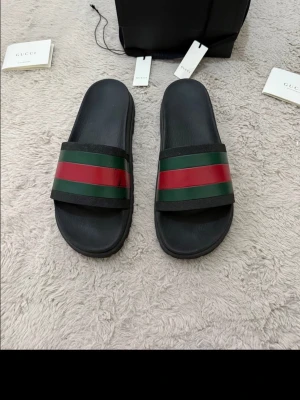 Gucci sandaler med röd och grön rand - JULREA! Klassiska Gucci-sandalerna. Riktigt fräscha, lite allmänt slitage och lite färglossning på högra sandalen vid ränderna - fortfarande i väldigt snyggt skick. Allt OG förutom kvitto, köpt i High end Sweden på Facebook. Mycket liv kvar i sandalerna. Storlek US 10 (44 EU).